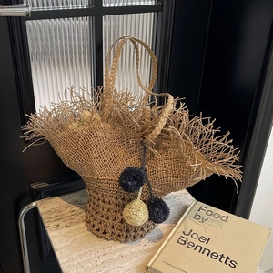 Elegante borsa tote in paglia intrecciata da donna con pompon decorativi su marmo
