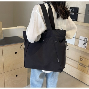 Detail of minimalist black fabric tote bag featuring side drawstring and logo tag on model