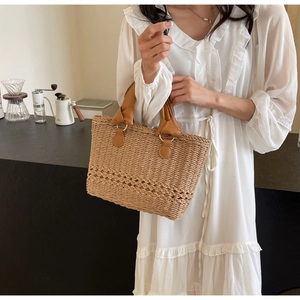 Detail of a straw tote bag featuring diamond hollow weave and brown leather handles