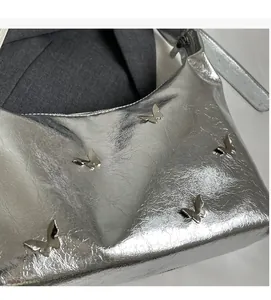 Detail of silver textured PU bag with metallic butterfly accents on soft pleated surface