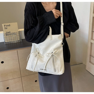 Close-up of white PU tote bag with ribbon bows and decorative zipper on a model