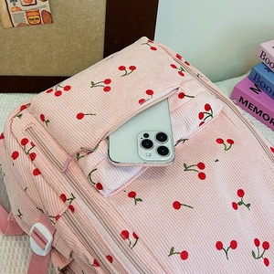 Détail du sac à dos en velours rose à cerises montrant la poche avant avec un smartphone