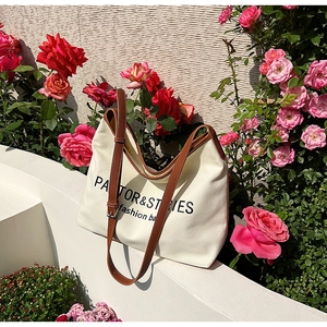 Minimalist canvas tote bag with brown leather straps placed on stairs near flowers