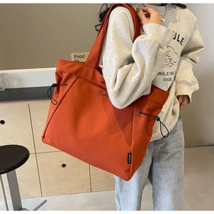 Macro detail of large orange canvas tote bag showing black side drawstring buckle
