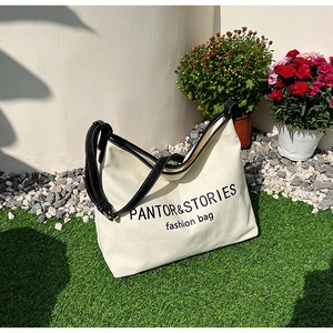 Minimalist canvas tote bag with black leather straps and fashion text on outdoor lawn