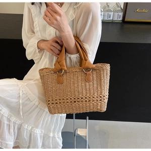 Detail of woven straw tote bag with brown leather handles and decorative hollow texture