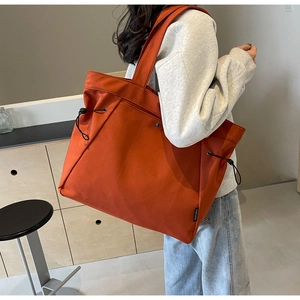 Detailed view of an orange canvas tote bag with side drawstring and black brand tag