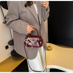 Detail of dark red PU crossbody bag with silver clasp and pearl butterfly charm decoration