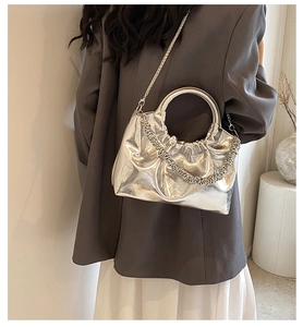 Detail of silver ruched handbag with metal ring handle and chain strap on model