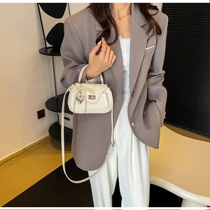 Close-up of cream PU handbag featuring pearl bow chain and silver heart pendant detail