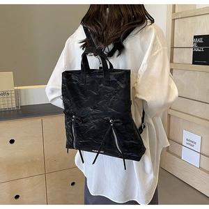 Detail of black pleated PU leather backpack featuring zipper accents and delicate bow ties