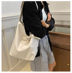 Detail of white PU leather tote bag featuring a textured finish and a delicate bow tie decoration