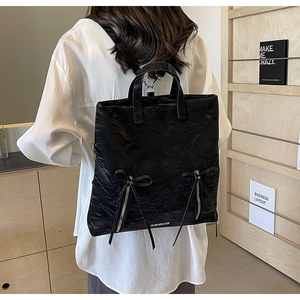 Detail of black pleated PU leather backpack with decorative bows and metal zippers