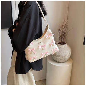 Close-up of a cream PU leather shoulder bag with pink silk bows and pearl charms
