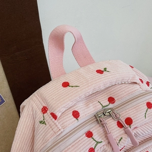 Détail d'un sac à dos rose en velours côtelé avec broderie cerise et doubles zips