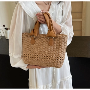 Detail of hand-woven straw tote bag with brown leather handles and hollowed-out texture