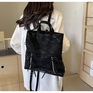 Close-up of black PU backpack with bow-decorated pockets and pleated leather texture