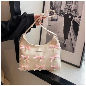 Detail of cream PU crescent bag featuring pink silk bows and hanging pearl pendants