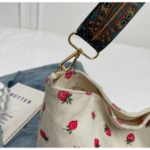Close-up of white corduroy strawberry tote bag with colorful bohemian woven strap