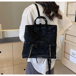Detail of black PU shoulder bag showing textured material and decorative bow accents