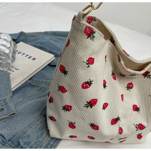 Detailed shot of cream corduroy bucket bag with red strawberry print and gold chain