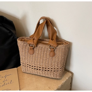 Handwoven straw tote bag with brown leather handles and gold rings on a stone surface