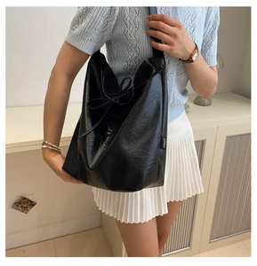Detail of black faux leather tote bag with side drawstring bow and textured pleats