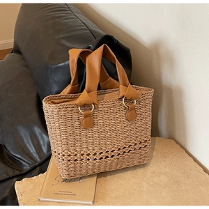Minimalist straw woven handbag with brown faux leather handles on a stone pedestal