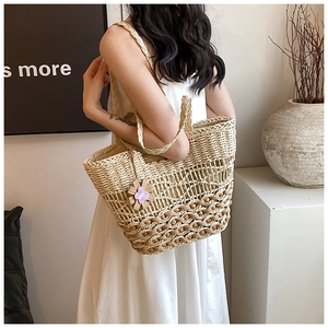 Detailed close-up of handmade straw tote bag with brown woven base and decorative purple flower
