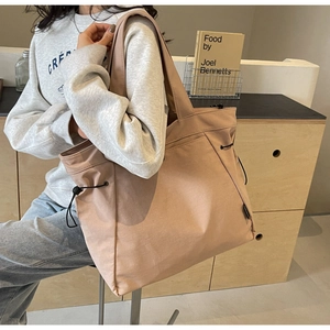 Detail of apricot canvas tote bag with side drawstring worn by a model in soft light