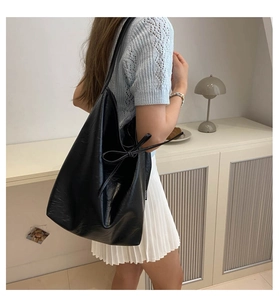 Detail of black PU leather shoulder bag featuring a decorative side bow tie design