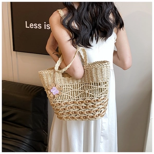 Detail of hand-woven straw tote bag with mesh design and purple floral charm on strap