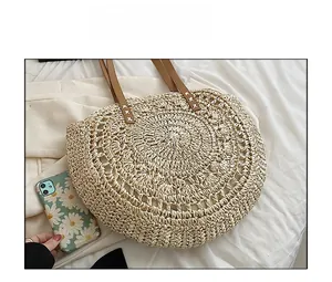 Detail view of large semicircular straw tote bag with brown leather handles and woven texture