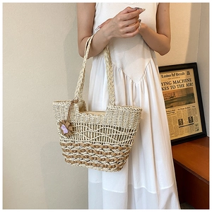 Detail of woven straw tote bag with contrast stitching and floral charm accessory