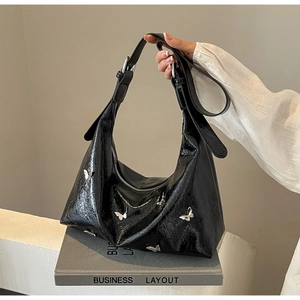 Detail of black patent leather crescent hobo bag with silver butterfly metal charms