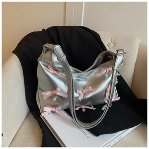 Silver PU leather shoulder bag with pink satin bows and white pearl charms on sofa