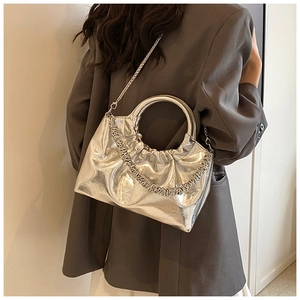 Detailed view of silver pleated cloud bag with round metal handle and chain strap on model