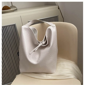 Off-white PU leather tote bag with drawstring details on a neutral leather chair