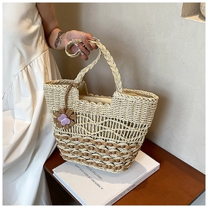 Detail of a two-tone straw tote bag with scalloped edges and purple flower charm accent
