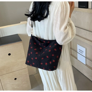 Close-up of black corduroy tote bag featuring strawberry embroidery and golden metal hooks