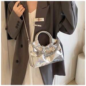 Close-up of metallic silver pleated handbag with chain strap styled with a grey blazer