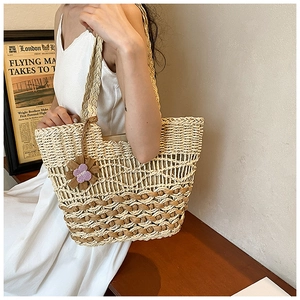 Detail of woven straw handbag featuring purple flower charm and rustic wave pattern