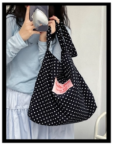 Detailed shot of a black canvas bag with white polka dots and a pink logo patch
