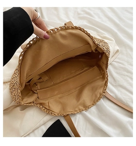 Detail view of woven straw bag interior with lining, zipper pocket and brown PU handle