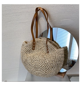 Detail of round straw tote bag with brown leather handles and cross-stitch reinforced straps
