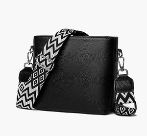 Detail of black pebbled leather bucket bag with geometric black and white woven wide strap