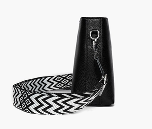 Detail of black lychee leather bucket bag with geometric black and white wide shoulder strap