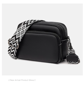 Detail of black lychee leather crossbody bag with dual zippers and geometric strap