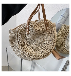 Detail of round straw tote bag featuring brown leather handles and woven texture