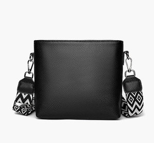 Detail of black pebbled leather bucket bag with geometric patterned wide strap and silver clips